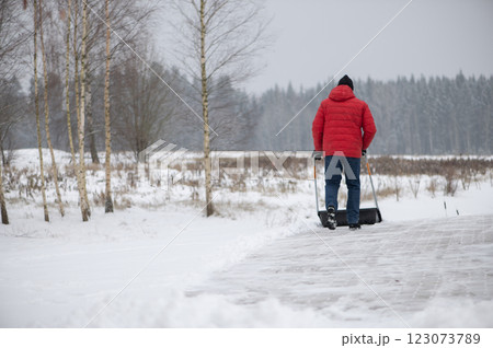 Rear view of man with a snow shovel cleans the pavement in the yard. Man shoveling snow after a winter storm. 123073789