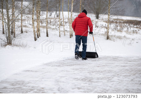Rear view of man with a snow shovel cleans the pavement in the yard. Man shoveling snow after a winter storm. 123073793