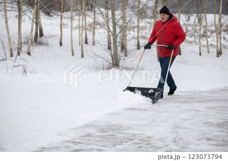Angry man with a snow shovel cleans the pavement in the yard. Man shoveling snow after a winter storm. 123073794