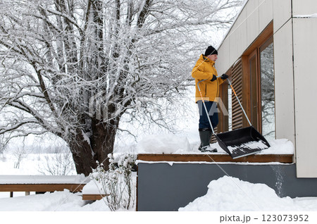 man in winter clothes with snow shovel cleaning snow from the terrace of the building man in winter clothes with snow shovel cleaning snow from the terrace of the building 123073952