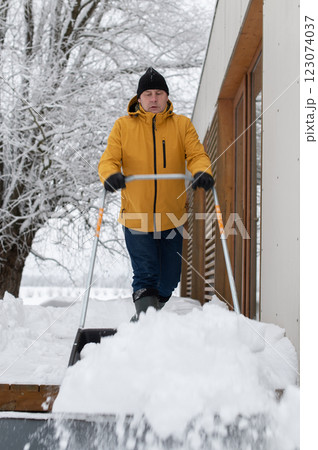 man in winter clothes with snow shovel cleaning snow from the terrace of the building man in winter clothes with snow shovel cleaning snow from the terrace of the building 123074037