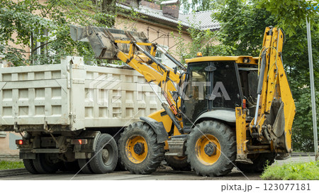 yellow tractor pours construction debris into the back of a dump truck 123077181