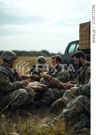 Soldiers in full gear sitting on grass, eating field rations together, sharing moment of camaraderie and resilience in outdoor military camp. 123077296