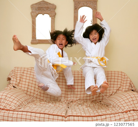 Two little asian judo gils jump on sofa 123077565