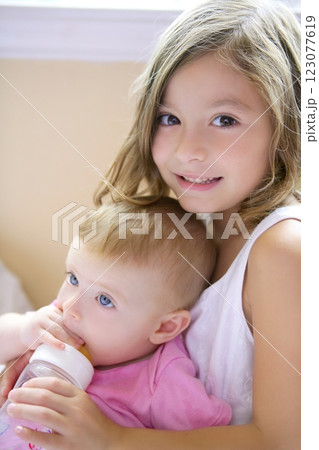 Toddler girl giving bottle of milk to baby sister 123077619