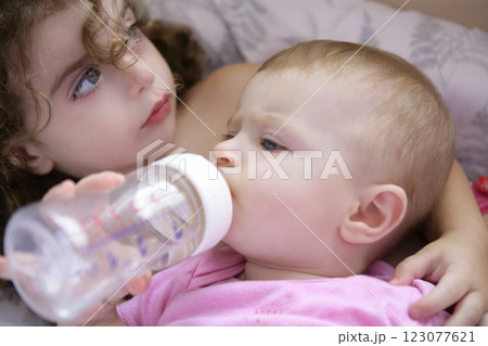 Toddler girl giving bottle of milk to baby sister 123077621