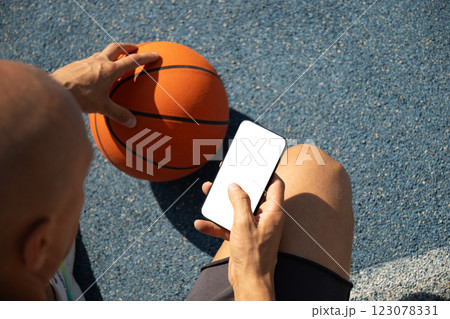 Basketball player using smartphone and texting social media during game interval, Outdoor training. View from above. Close up. 123078331