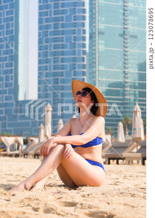 A Stylish Woman in a Blue Swimsuit, Hat, and Sunglasses Exudes Confidence and Elegance While Relaxing on an Urban Beach, Enjoying the Sun and Vibrant Atmosphere of City Life, Perfectly Capturing the A Stylish Woman in a Blue Swimsuit, Hat, and Sunglasses Exudes Confidence and Elegance While Relaxing on an Urban Beach, Enjoying the Sun and Vibrant Atmosphere of City Life, Perfectly Capturing the 123078695