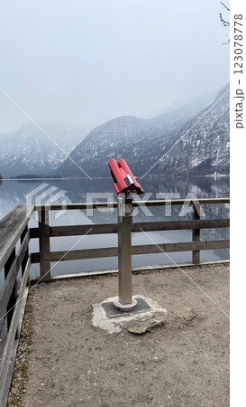 Red Viewing Binoculars Overlooking a Serene Lake Hallstatt and Misty Alpine Mountainous Backdrop Red Viewing Binoculars Overlooking a Serene Lake Hallstatt and Misty Alpine Mountainous Backdrop 123078778
