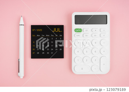 July 2025 calendar and white calculator with pen on pink background. July 2025 calendar and white calculator with pen on pink background. 123079189