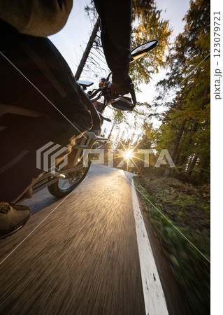 Driver riding motorcycle on empty road during sunset , view from the passenger side 123079721