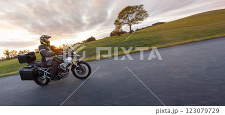 Driver riding motorcycle on empty road during sunset, autumn mountains 123079729