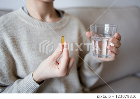Female taking fish oil capsule with water in cozy home setting 123079810