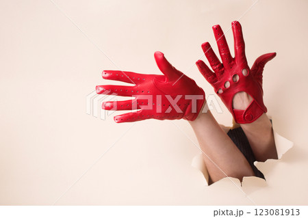 A woman's hands in a red leather gloves pushed through a hole A woman's hands in a red leather gloves pushed through a hole 123081913