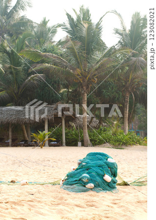 Green net with large floats lies on the shore near the ocean, with palm trees in the background Green net with large floats lies on the shore near the ocean, with palm trees in the background 123082021