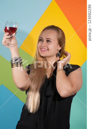 Beautiful blonde in a black dress holding a glass of red wine and looking at the drink and smiles Beautiful blonde in a black dress holding a glass of red wine and looking at the drink and smiles 123082286
