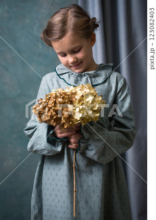 A girl is holding a branch with a hydrangea flower. She is wearing a green vintage dress A girl is holding a branch with a hydrangea flower. She is wearing a green vintage dress 123082403