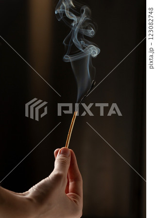 A woman's hand holds a long match that is extinguished and smoking 123082748