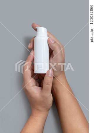 Female hands holding white cosmetic one pump bottle over grey top view, mockup, copy space Female hands holding white cosmetic one pump bottle over grey top view, mockup, copy space 123082866