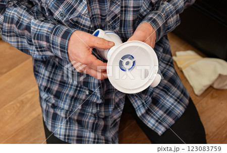 An elderly man focuses on assembling plumbing components for the kitchen and bathroom on a wooden floor. An elderly man focuses on assembling plumbing components for the kitchen and bathroom on a wooden floor. 123083759