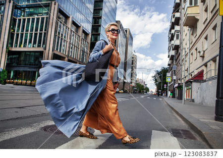 Stylish Woman Walking City Street In Fashionable Attire, Wearing Long Beige Silk Dress, Blue Cape Coat, Carrying Black Handbag, Sunglasses And Trendy Animal print ballet flats 123083837