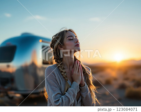 Young woman praying at sunset in the desert near her camper trailer 123084071