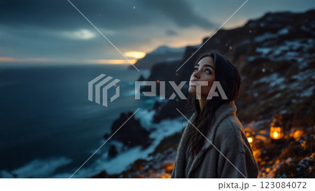 Young woman looking up at the sky while snowing on a cliff at sunset 123084072