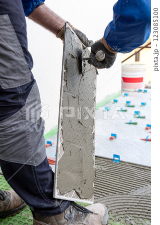 Tiler at work installing new floor with tiles. Construction. 123085100