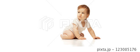 Banner. Baby in onesie, sitting with one hand on floor and head turned to side against white background with negative space to insert text. Banner. Baby in onesie, sitting with one hand on floor and head turned to side against white background with negative space to insert text. 123085176