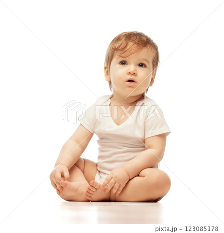 Portrait of of little, curious baby, dressed white onesie, sitting and gazing upward with wide eyes and relaxed posture against white background. Portrait of of little, curious baby, dressed white onesie, sitting and gazing upward with wide eyes and relaxed posture against white background. 123085178