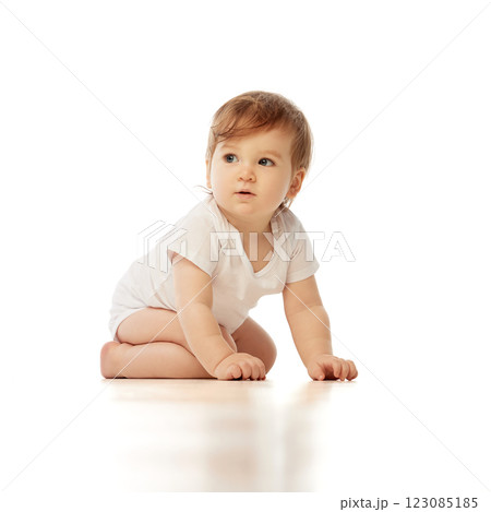 Little, charming baby, dressed white onesie, kneeling and gazing sideways with curious expression against white background. 123085185