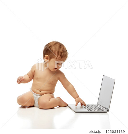 Portrait of little baby in diaper sitting and reaching out to touch laptop keyboard while looking at screen against white background. Portrait of little baby in diaper sitting and reaching out to touch laptop keyboard while looking at screen against white background. 123085189