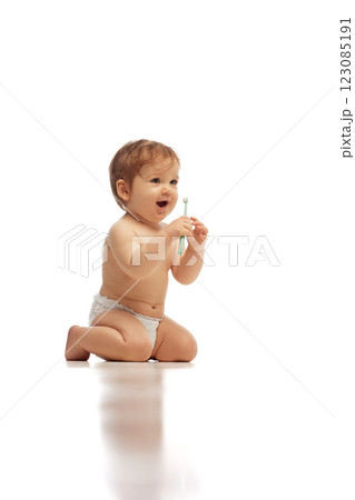 Portrait of little baby, in diaper, kneeling and playfully holding toothbrush while laughing against white background. Portrait of little baby, in diaper, kneeling and playfully holding toothbrush while laughing against white background. 123085191