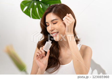 Asian woman demonstrating skincare routine with facial serum in a bright white background Asian woman demonstrating skincare routine with facial serum in a bright white background 123085960