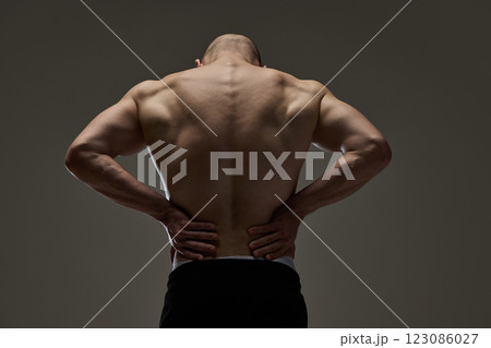 Close-up of male model's muscular, healthy back with hands resting on waist against dramatic lighting. Concept of natural beauty. Close-up of male model's muscular, healthy back with hands resting on waist against dramatic lighting. Concept of natural beauty. 123086027