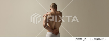 Banner. Masculine man, dressed underwear, standing with back arched and arms crossed in emotional movement against soft- beige studio background. Banner. Masculine man, dressed underwear, standing with back arched and arms crossed in emotional movement against soft- beige studio background. 123086039