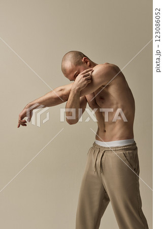 Athletic male model, dressed stylish beige pants, stretching arm with dynamic posture against neutral beige studio background. 123086052