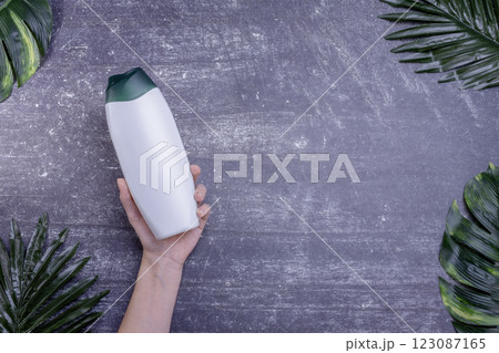 Female hand holding shower gel bottle on gray background with leaves 123087165