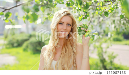 Beautiful blonde young woman in spring blooming garden on a sunny day against flowers trees 123087188