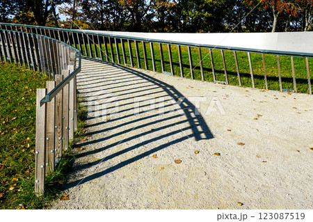 Metal railing casting long symmetrical shadow lines on the surface of a gravel path in sunny weather Metal railing casting long symmetrical shadow lines on the surface of a gravel path in sunny weather 123087519