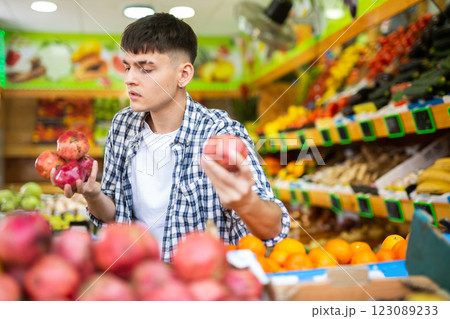 Young man chooses pomegranate fruit on counter of grocery store Young man chooses pomegranate fruit on counter of grocery store 123089233