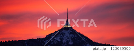 Jested Mountain stands majestically against a vibrant winter evening sky in Czechia. The snow-covered landscape glows as the setting sun paints the horizon in warm hues. 123089500