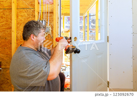 Craftsman uses screwdriver to install door handle in house under construction 123092670