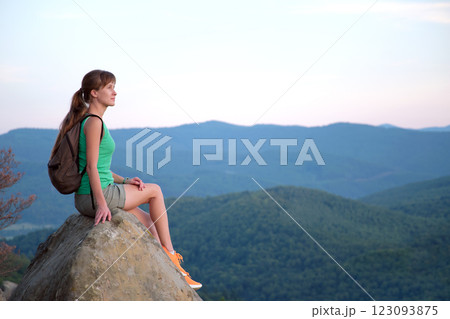 Sportive female hiker sitting alone taking a break on hillside trail. Lonely woman enjoying view of summer nature from rocky cliff on wilderness path. Active lifestyle concept 123093875