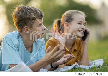 Sad teen friend being ignored by another outdoors while she is talking happily on mobile phone and paying no attention. Friendship problems concept Sad teen friend being ignored by another outdoors while she is talking happily on mobile phone and paying no attention. Friendship problems concept 123094029