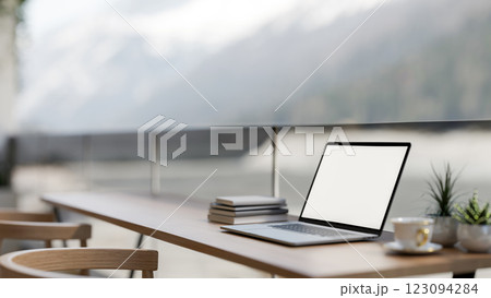 A laptop on the wooden table in the coffee shop, the sitting spot beside glass partition. 123094284