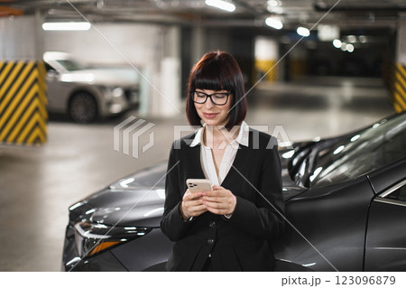 Caucasian woman in suit using smartphone in indoor car park. Business setting with focus on communication and connectivity. 123096879