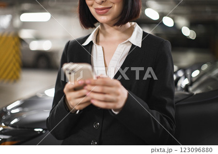 Young female businesswoman in indoor car park holding smartphone, dressed in professional attire, engaging in communication. Caucasian and confident displaying focus and dedication in business setting Young female businesswoman in indoor car park holding smartphone, dressed in professional attire, engaging in communication. Caucasian and confident displaying focus and dedication in business setting 123096880