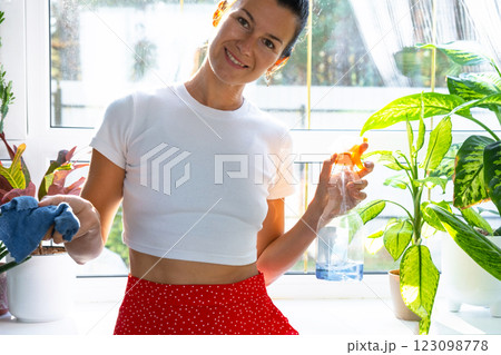 Portrait Woman with detergent, manually washes window of house with rag cleaner and mop inside interior with home plants. Restoring order and cleanliness in the spring, cleaning servise. 123098778