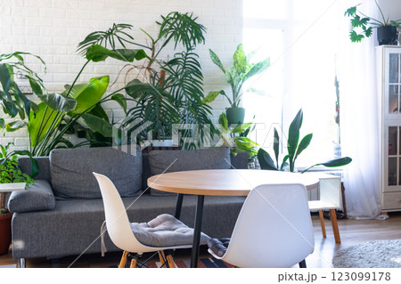 Modern loft-style village interior of house with large potted plants, gray sofa, empty round table, a striped rug, and large windows. 123099178